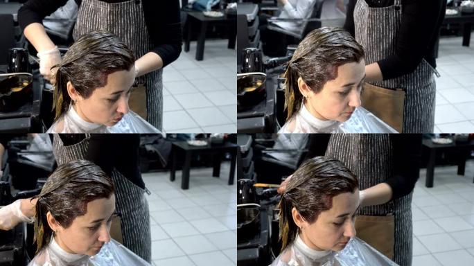 理发店的染发。一个成年女孩坐在理发店里，理发师在她的头发上涂上油漆。头发护理。特写。4 k.25 f