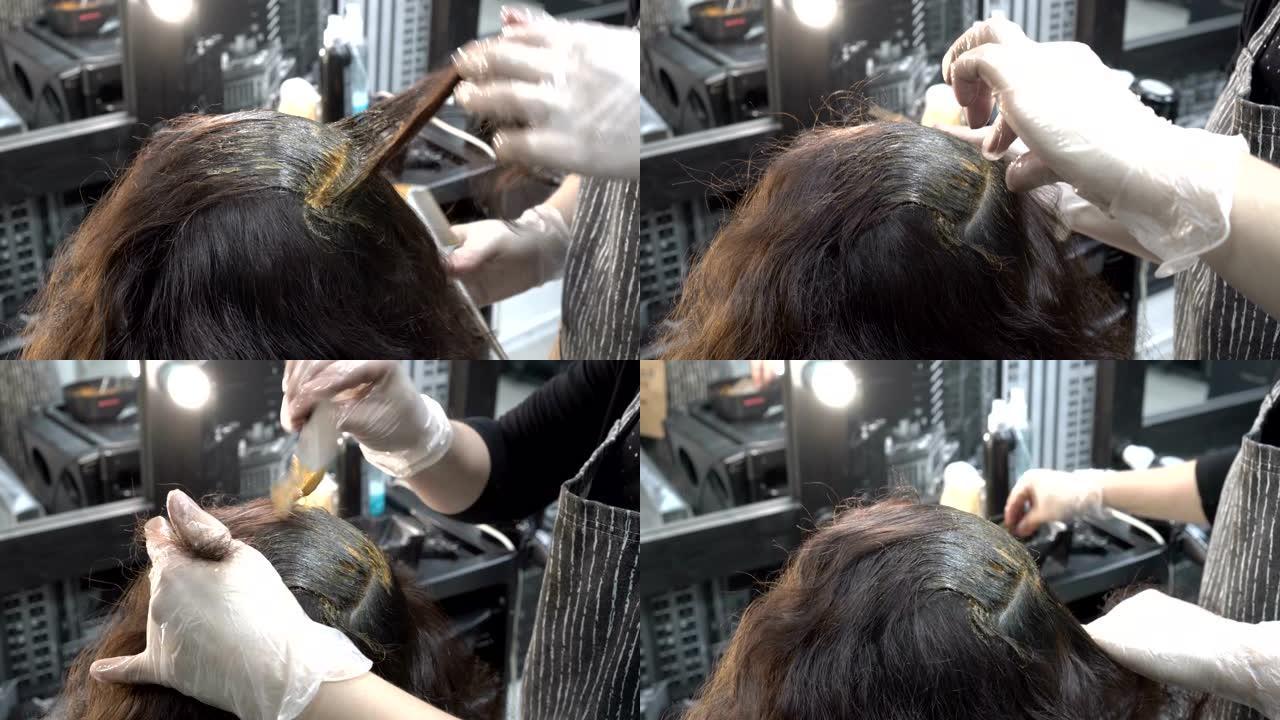 理发师-发型师在理发店画头发。她将女孩的头发分成几束，然后用刷子在上面涂上油漆。头发护理。特写。从顶