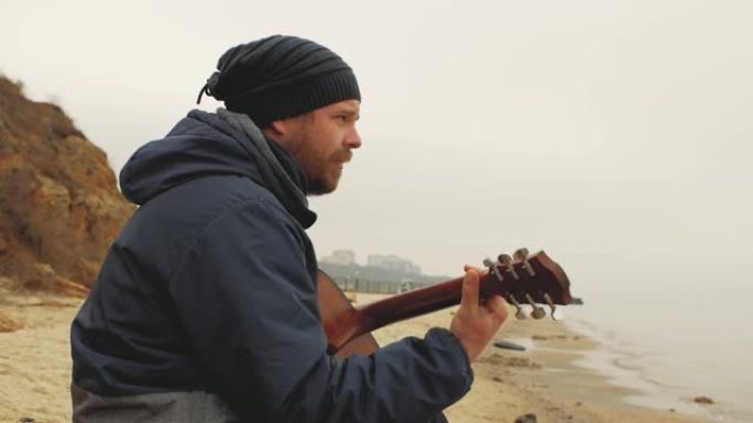 一个留着胡子的家伙坐在海边的石头上弹吉他