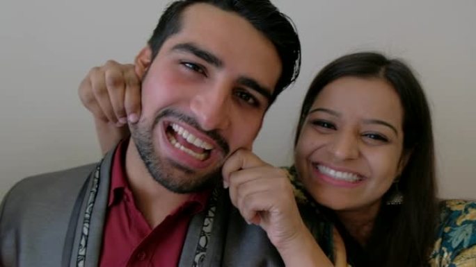 印度年轻夫妇看着相机pov并拍照，而妻子则以顽皮的方式拉着丈夫的脸颊，手持设备稳定下来