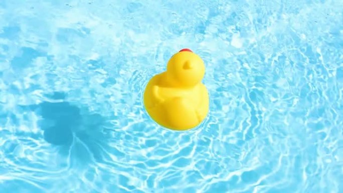 在夏日的灯光下，一只黄色的橡皮鸭随意地漂浮在水池的波光粼粼而清澈的水面上