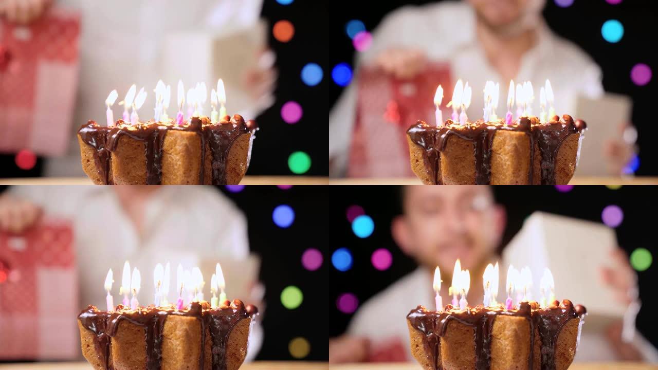 充满生日蜡烛的美味巧克力蛋糕。男人在生日聚会上微笑跳舞。生日礼物，特写4k镜头