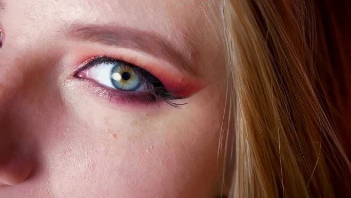 迷人的女性蓝眼睛化妆特写，粉色阴影和金色眼线。右眼看着相机
