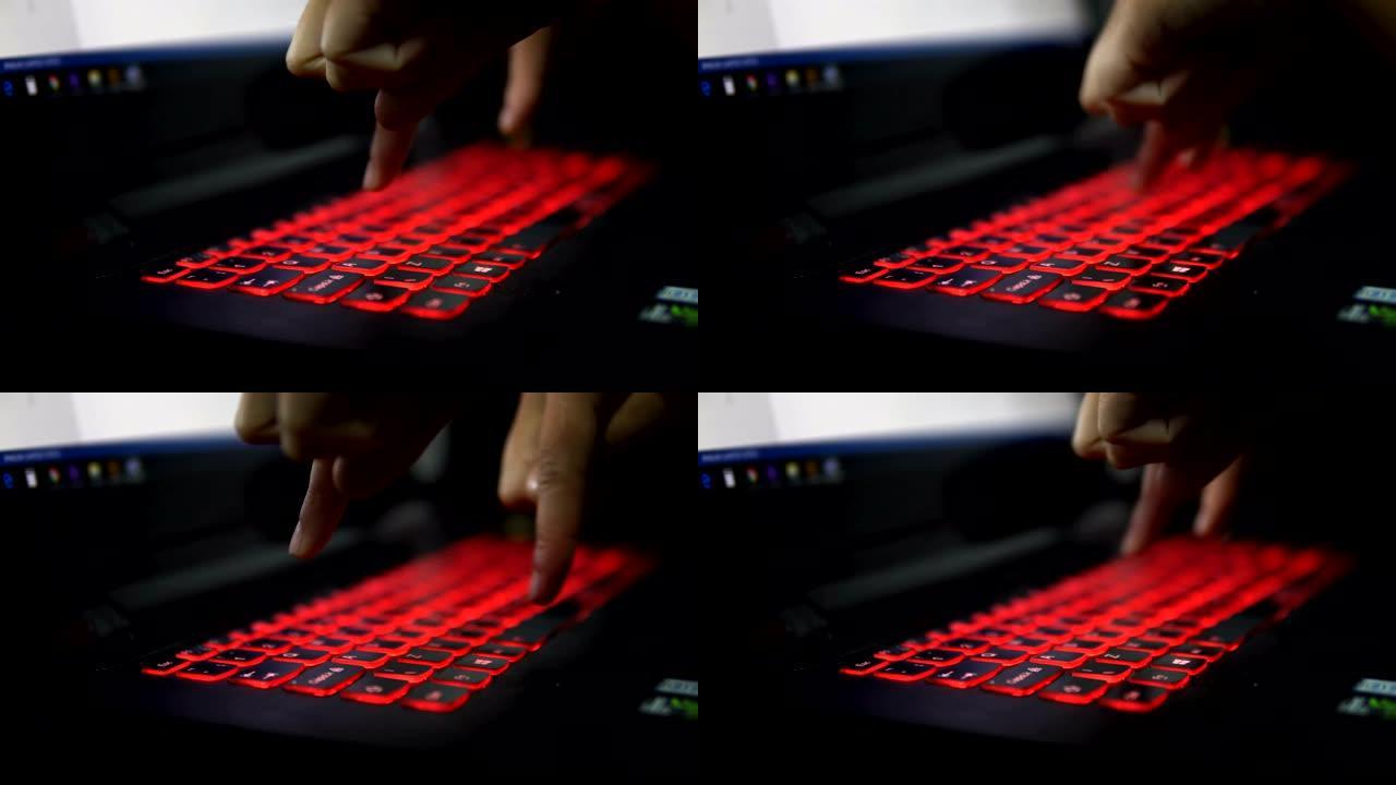 在黑暗中，用两个手指在带有红色键盘的笔记本电脑上打字。特写剪辑。人造光。深夜工作。黑客。饼干。工程师