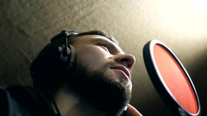 耳机男歌手在sound studio的麦克风中唱歌。年轻人在情感上录制新歌。创意音乐家的工作。展示商
