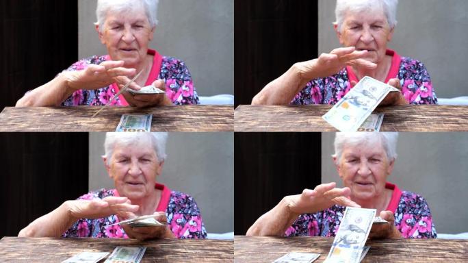 快乐的祖母手里拿着一捆钱，把外币撒在桌子上的肖像。老微笑的女人把100美元的钞票扔在桌子上。关闭慢动