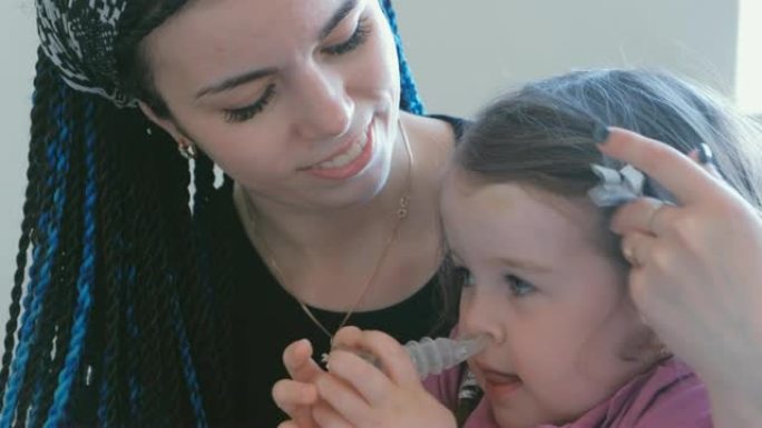 可爱的小女孩和妈妈一起通过吸入器面罩吸气。使用雾化器和吸入器进行治疗。