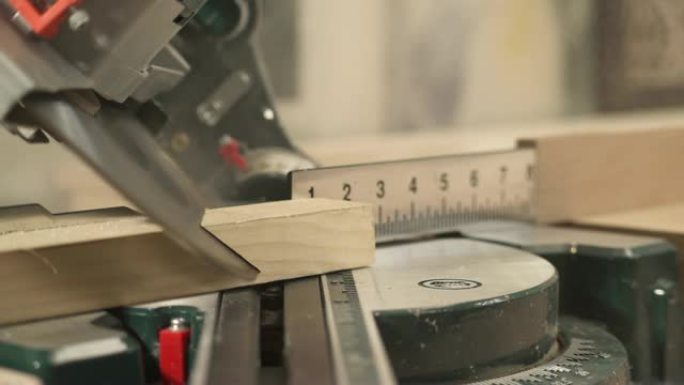 斜切锯的前视图，在锯末飞行的情况下以选定的角度切割工件。一只手正在拿切割的工件