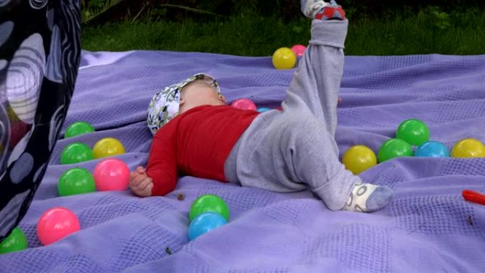 女婴大笑，踢腿，躺在花园里的垫子上。4K
