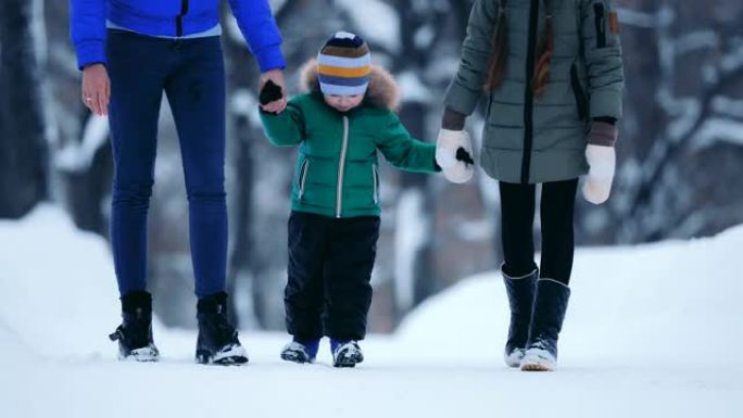 快乐的婴儿与他的妹妹和母亲在冬季公园散步。一家人走在雪道上，每个人都牵着手。