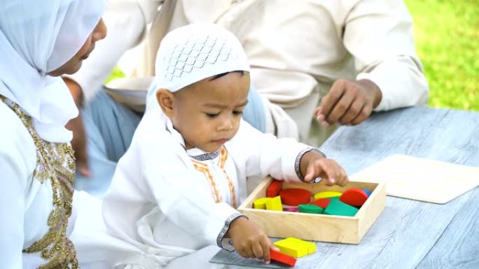 从侧面看高角度: 穆斯林家庭带着儿子早上在公园里用木制玩具学习
