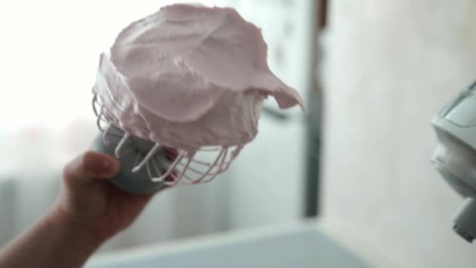 一位女性糖果店的手从搅拌机上握着钢打蛋器，上面覆盖着粉红色的草莓棉花糖。