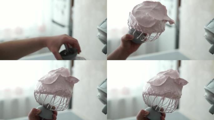 一位女性糖果店的手从搅拌机上握着钢打蛋器，上面覆盖着粉红色的草莓棉花糖。