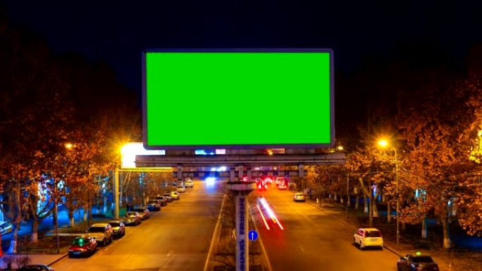 带有绿色色度键的广告牌，背景是长时间曝光的快速行驶的汽车的城市夜景。相机移开了。