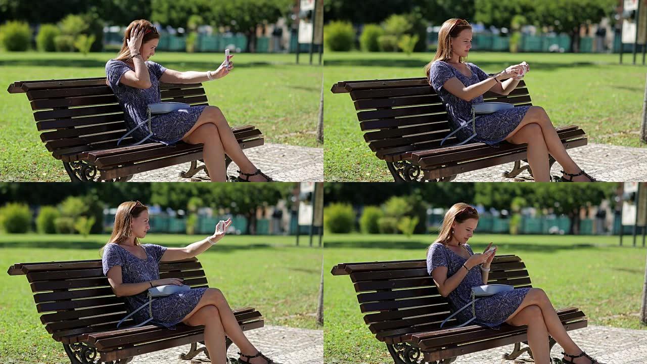 年轻漂亮的女人让自拍手拿手机坐在公园的长凳上