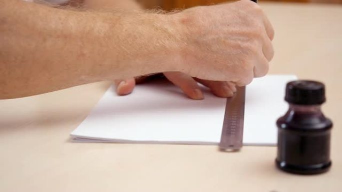 男人的手用尺子和毛笔在白色空白上画一条线。近距离拍摄。侧视图。设计师工作场所视图。准备书法刻字。背景