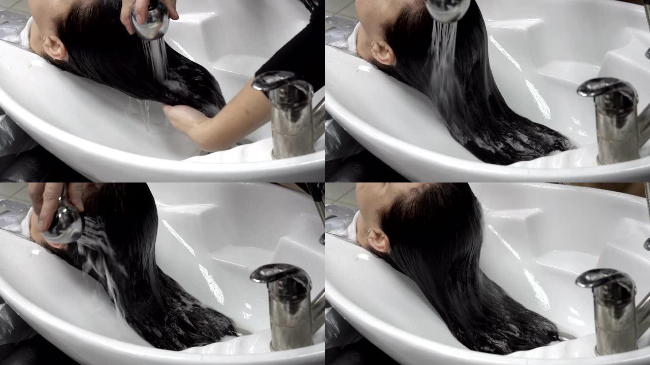 理发师在理发店的淋浴间里用一股强烈的水流在白色的水槽上冲洗女孩的头发。头发护理。特写。4K。