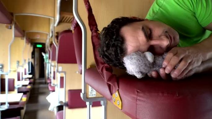 英俊的男人和玩具泰迪熊在火车上睡觉。劳累的工人学生下班后睡觉，辛苦一天，压痛依恋