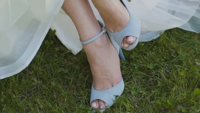 女人穿上鞋子手靠近浅层景深。新娘穿着华丽的白色礼服在豪华的高跟凉鞋上系拉链，为婚礼上的舞蹈做准备