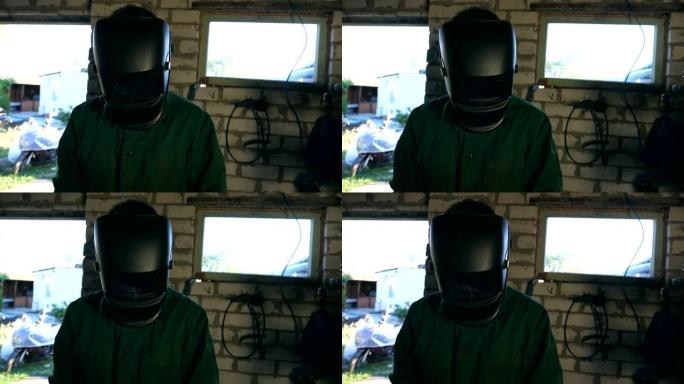 男性机械师使用防护面罩工作的特写镜头。穿着工作服的人在车库或车间工作。为了安全，盖伊戴着焊接面具。努