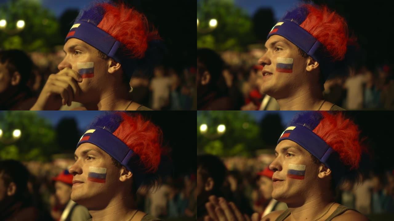 俄罗斯球迷脸上涂着颜料紧张地观看足球比赛，体验。