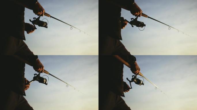 日落时分，渔夫在湖上钓鱼。一个穿着黑色背心和绿色帽子的渔夫用竹柄在纺纱上捕捉到掠食性鱼。