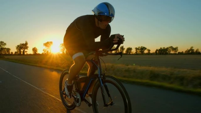 一名骑自行车的人在日落/日出时沿着道路用力推。