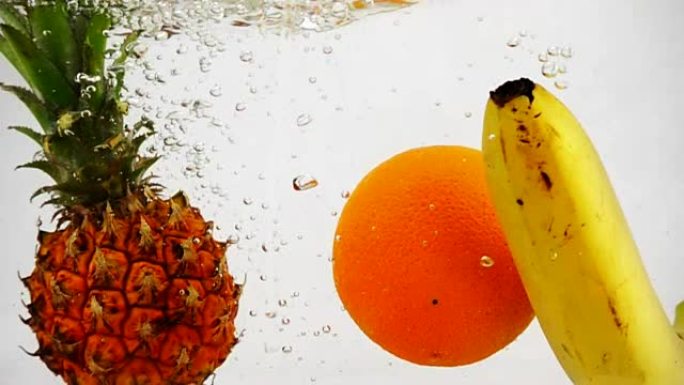 菠萝、橘子和香蕉落到水里，里面有很多小气泡。孤立的白色背景上的水果。