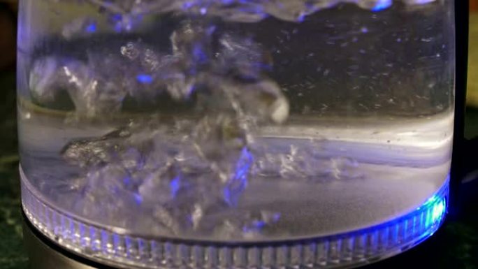 带有沉淀物的水在带有蓝光的透明电热水壶中沸腾特写