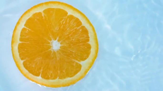 一块新鲜的切成薄片的橙子掉入水中，慢动作拍摄