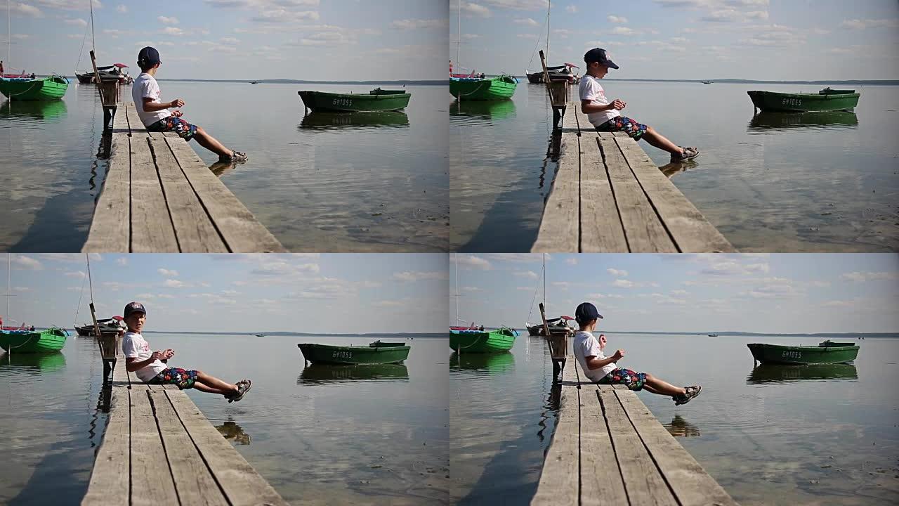 男孩在船附近的码头上的河里洗脚