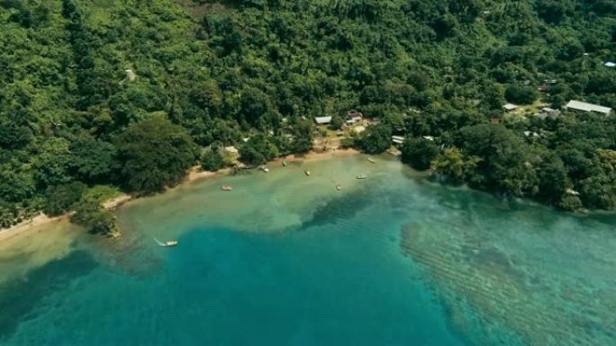 航拍无人机图像显示一个偏远岛屿上的南太平洋村庄，那里有一个美丽的珊瑚礁和郁郁葱葱的热带雨林丛林，同时