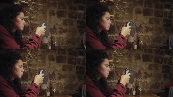 西班牙裔年轻女性发短信并使用手机在餐厅用餐