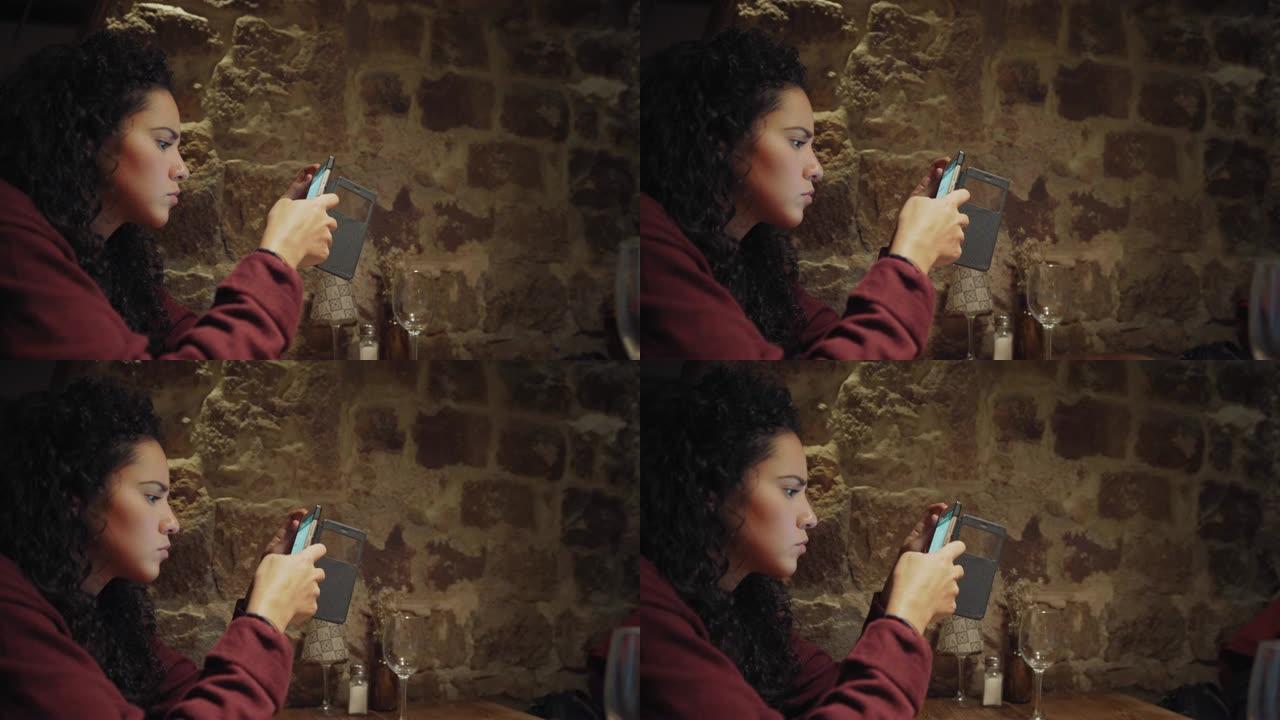 西班牙裔年轻女性发短信并使用手机在餐厅用餐