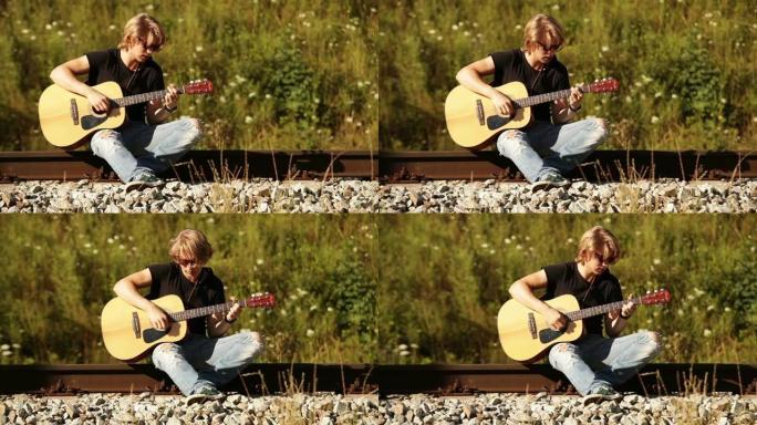 吉他手坐在铁轨上并在吉他上弹奏和弦的滑动镜头