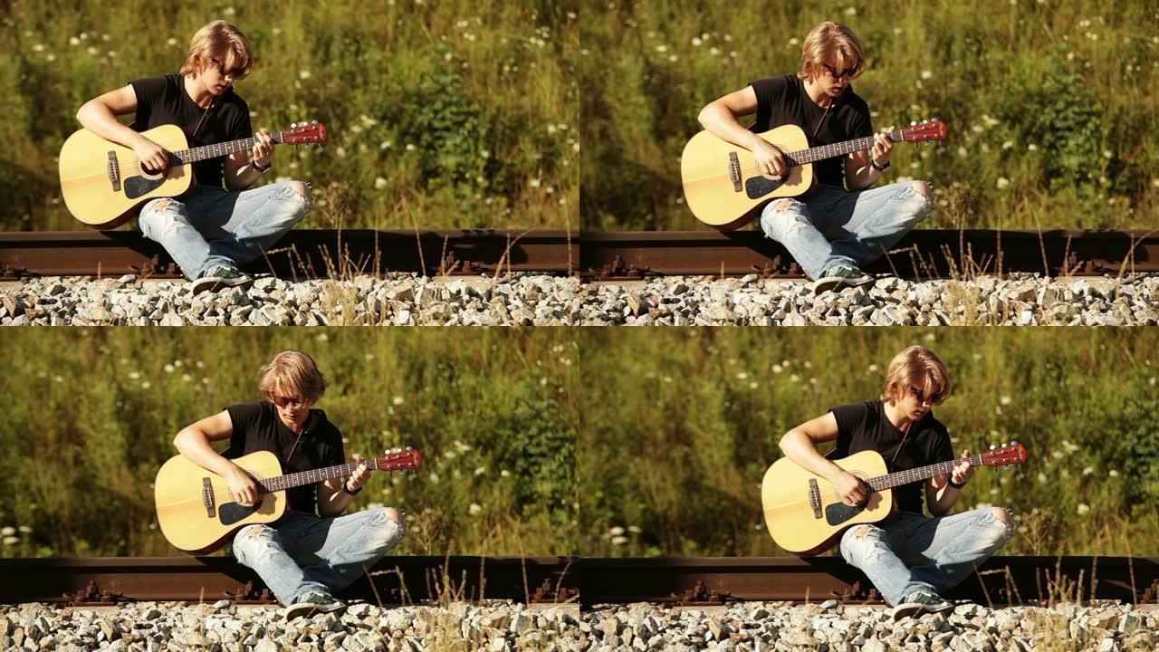 吉他手坐在铁轨上并在吉他上弹奏和弦的滑动镜头