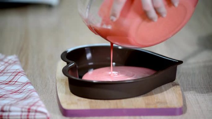 将粉色慕斯倒入心形模具中。糖果店在厨房里做慕斯蛋糕。