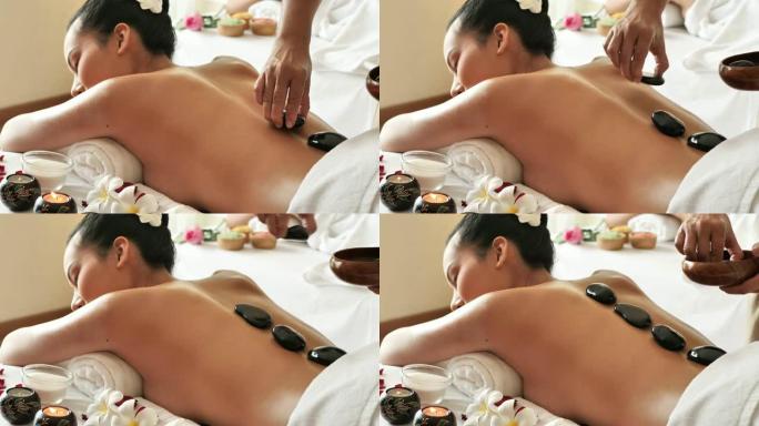 年轻的亚洲女人躺在床上放松得到热石按摩水疗沙龙。身体护理、皮肤护理、健康理念。4k视频慢动作