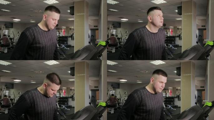 胖子在健身房的跑步机上锻炼