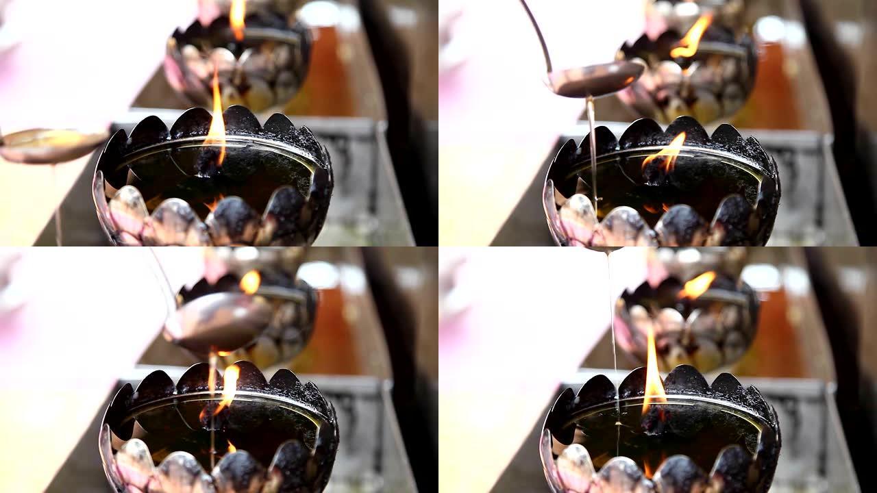 女孩的手用小钢包舀油，倒在泰国清迈寺庙里的一排油莲花形灯上。