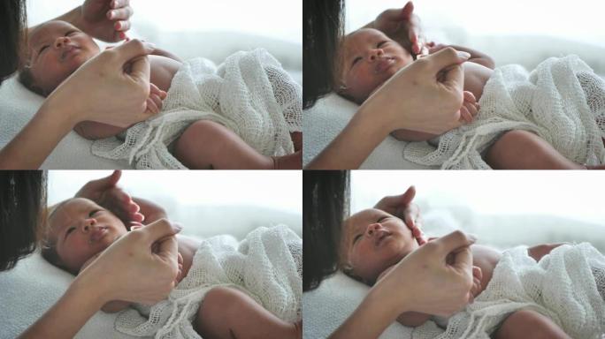 母亲牵着手亚洲女性新生婴儿躺在床上，早晨晒太阳。可爱的小女孩三周大。微笑，哭泣，扭动，爱情，家庭，束