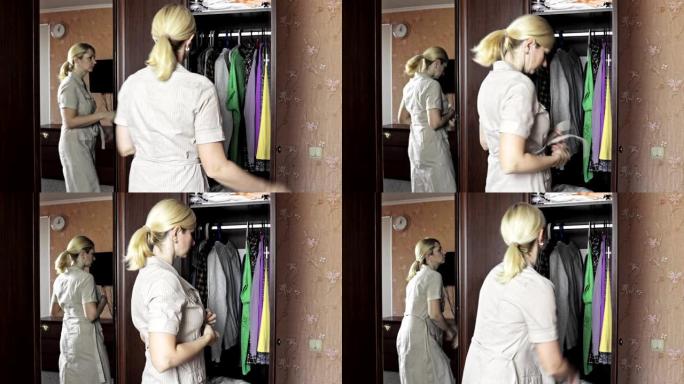 年轻的金发女子站在家里打开的衣柜前，解开她的家装，以便换衣服
