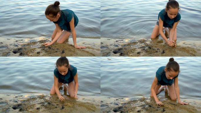 一个孩子，一个年轻的女孩，在日落时在河岸上建造一座沙堡。她坐在水边，用手耙沙。肖像。特写。4 k.2