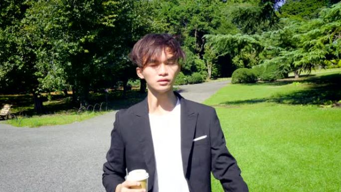 年轻成功的日本商人穿着西装，匆忙散步时喝咖啡-模特发布