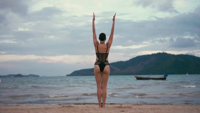 穿着黑色泳衣和医用防雾面具在海边练习瑜伽的白人妇女