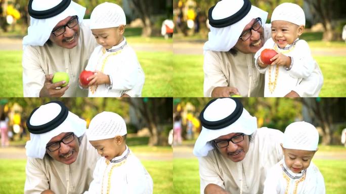 穿着传统服装的开朗的穆斯林祖父让儿子尝试吃苹果