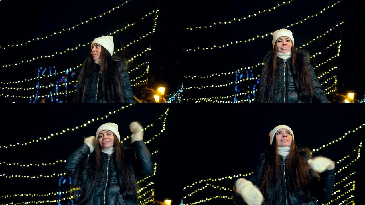 美丽的女孩微笑着在冬天穿过夜巷。街道上装饰着灯饰花环。摄像机的底视图。