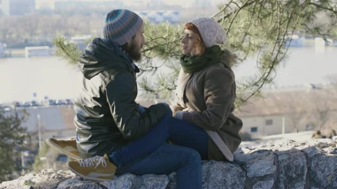 恋爱中的年轻夫妇坐在石墙上