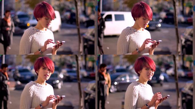 漂亮的粉红头发女孩的肖像用智能手机在模糊的街道背景上守望者，转向相机。