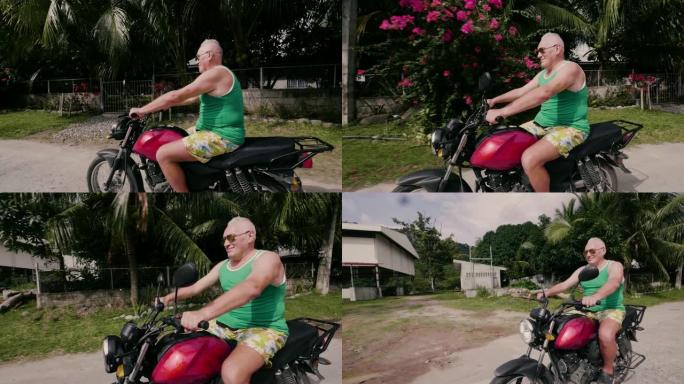暑假期间在乡下开摩托车的老人。戴墨镜的高级男子在旅行时在热带村庄的街道上骑摩托车。